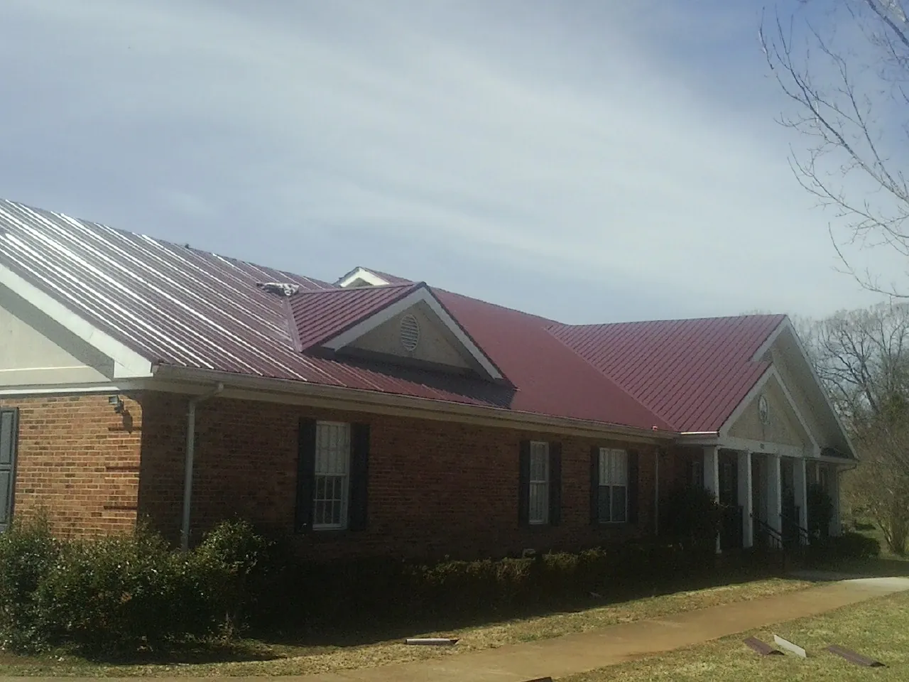 Red metal roof with gabled entries on a long brick building, from a Hail Damage Roof Repair job in Jonesboro