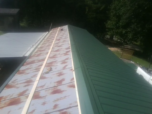Old rusted panels beside newly installed green metal roofing — Wind Damage Roof Repair by Roofing Brothers in Jonesboro