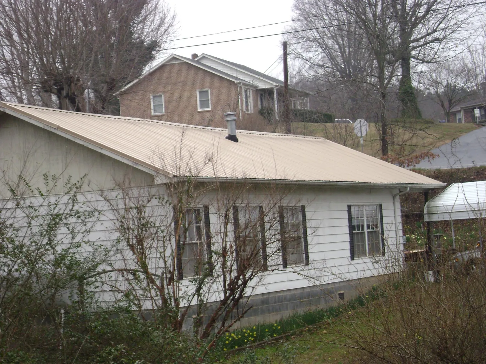 Tan metal roof on a white sided house set into a hillside — Commercial Roofing by Roofing Brothers in Jonesboro
