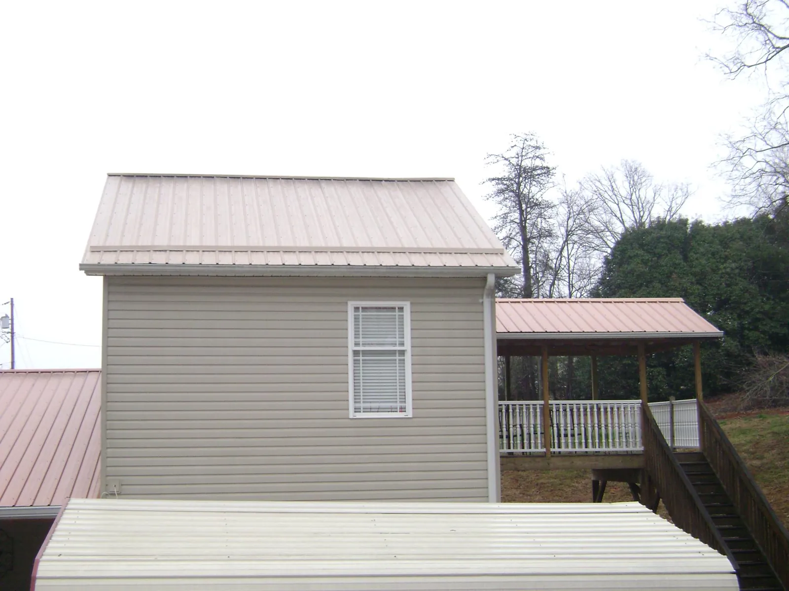Tan metal roofs on a two story addition and attached porch, from a Roof Replacement job in Jonesboro
